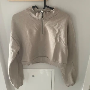 Beige croppad tröja från Nelly - Säljer en superfin beige croppad tröja från Nelly. Den har en dragkedja framtill och är långärmad med ribbade detaljer vid kragen och ärmsluten. 