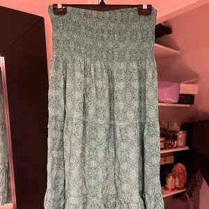 Grön mönstrad kjol - Snygg grön kjol med ett detaljerat mönster. Kjolen har en elastisk midja som ger en bekväm passform. Står inte märke eller storlek men skulle säga att den passar någon som är ca 160cm lång och från XS-M i midjan då den är väldigt stretchig
