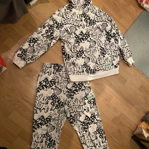 Svartvit mönstrad mjukisbyxa från Divided. Stolek i hoodie XS. 100kr för hoodien. Byxorna 150. - Coola svartvita mjukisbyxor med graffiti-inspirerat mönster från Divided. Byxorna har elastisk midja och muddar vid bensluten för en bekväm passform. Perfekta för en avslappnad stil med en touch av streetwear.