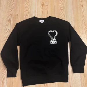 Svart sweatshirt från Ami Alexandre Mattiussi - Snygg svart sweatshirt från Ami Alexandre Mattiussi med ett unikt hjärtmönster på bröstet. Perfekt för en stilren och avslappnad look. Tröjan har långa ärmar och en klassisk rund halsringning.