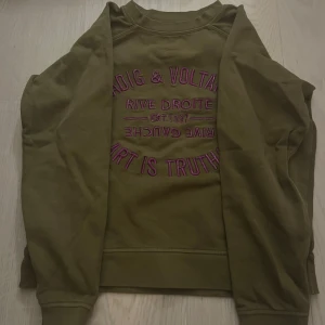 Olivgrön sweatshirt med tryck - Säljer en olivgrön sweatshirt med tryck i lila och rosa på framsidan. Tröjan har långa ärmar och en rund halsringning. Säljer den då jag inte andvänt den nästan helt oanvänd❤️priset kan diskuteras 