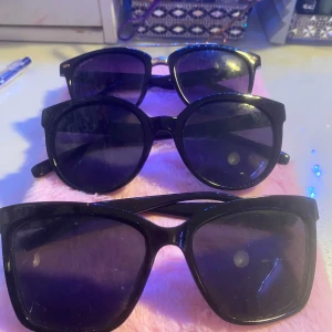 Tre par svarta solglasögon - Säljer tre par svarta solglasögon i olika stilar. Ett par har en rund form, ett annat har en mer fyrkantig design och det tredje paret har en klassisk wayfarer-stil. Perfekta för att komplettera din look med en touch av mystik. 