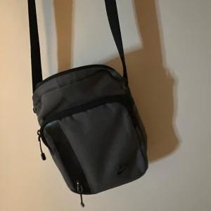 Svart axelväska från Nike - Snygg och praktisk svart axelväska från Nike med justerbar rem och dragkedja. Perfekt för att bära med sig 