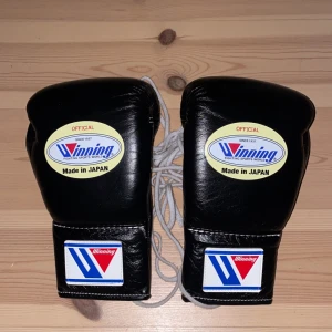 Svarta boxningshandskar från Winning - Säljer ett par svarta boxningshandskar från Winning, tillverkade i Japan. Handskarna har snörning och är märkta med 8 oz. Perfekta för träning och tävling.