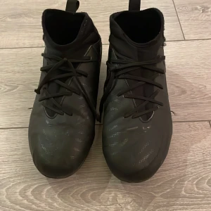 Svarta fotbollsskor från Nike - Snygga svarta fotbollsskor från Nike med snörning och en diskret vit Nike-logga på sidan. Perfekta för fotbollsplanen med en stilren design och bra passform.