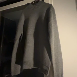 Grå stickad tröja från Sandö. oanvänd!!! - Säljer en stilren grå stickad tröja från Sandö i storlek M. Tröjan har en klassisk design med ribbad krage och muddar, perfekt för kyligare dagar.     Helt oanvänd!!!