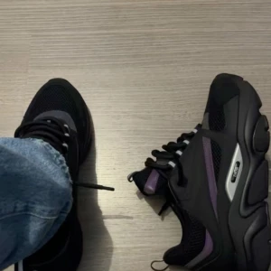  Dior b22 - Snygga svarta sneakers från Dior med detaljer i lila och silver. Skorna har en robust sula och snörning framtill. Perfekta för en stilren look. De är storlek 42 säljer pga de var inte den stil jag tänkte mig när jag köpte skorna pris kan diskuteras OBS ENDAST SERIÖSA KUNDER