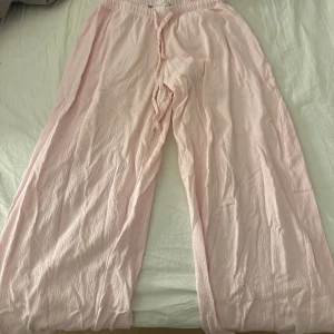 Rosa pyjamas byxor. - Säljer ett par rosa pyjamasbyxor. De har en loose passform och är perfekta för en avslappnad stil. Byxorna har en elastisk midja med snörning för extra komfort. Från Lager 157.