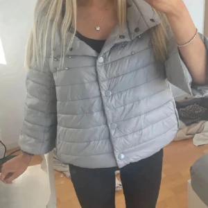 Grå pufferjacka med pärlor - Herno liknande jacka! Snygg grå pufferjacka med trekvartsärm och dekorativa pärlor på axlarna. Jackan har knappar framtill och en hög krage för extra stil. Köpte precis här på Plick men den passade tyvärr inte mig men annars är den hur fin som helst 🥰lånade hennes bilder🥰