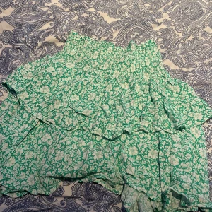 Grön blommig kjol - Söt grön kjol med vitt blommönster och volanger. Perfekt för en somrig look med sin korta längd och luftiga design.