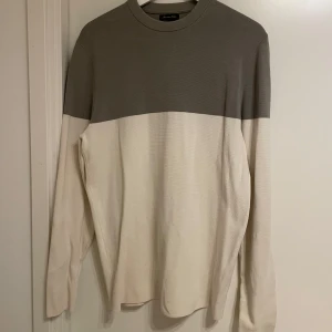 Tvåfärgad tröja från Massimo Dutti - Snygg långärmad tröja från Massimo Dutti i en stilren tvåfärgad design. Överdelen är grå och nederdelen är beige. Tillverkad i exklusiv bomull för en bekväm känsla. Perfekt för en avslappnad men stilfull look.