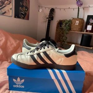 Adidas gazelle - Snygga Adidas fotbollsskor i vitt med svarta detaljer och klassiska tre ränder. Skorna har en unik tysk design med texten 'Deutscher Fussball Bund' på plösen. Perfekta för fotbollsälskare!