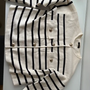 Randig kofta från Massimo Dutti - Snygg randig kofta från Massimo Dutti i svart och vit med dekorativa knappar framtill. Koftan har två fickor och en klassisk design som passar perfekt för både vardag och mer uppklädda tillfällen. Använd vid få tillfällen, säljs pga att den blivit liten på mig.