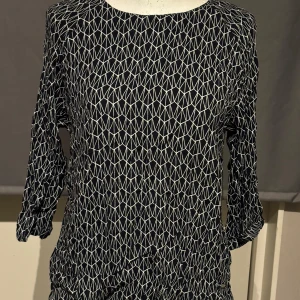 Svart och vit mönstrad tröja från Dobber - Snygg svart tröja med vitt geometriskt mönster från Dobber. Tröjan har långa ärmar och en rund halsringning, perfekt för en stilren look. Passar bra till både jeans och kjol.