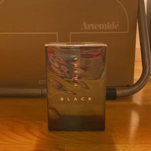 Prada Black Parfym - Elegant parfymflaska från Prada i en stilren svart design. Flaskan har en glansig yta med märkets namn i guldtext. Perfekt för den som söker en sofistikerad doftupplevelse.