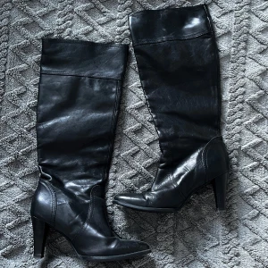 Stövlar  - Väldigt snygga svarta stövlar i skinn med hög klack och spetsig tå som går upp till knäna. Har gångveck.