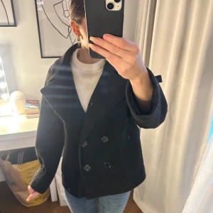 Svart kappa från Design by Si - Snygg svart kappa från Design by Si med dubbelknäppning och bred krage. Perfekt för kyligare dagar och ger en stilren look. Passar bra till både jeans och mer uppklädda outfits. Har dock en lite defekt som är inuti ena ärmen därav inget som syns! Pris diskuteras vid snabb affär! 