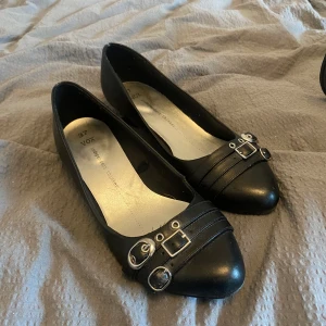 Svarta kittenheels - Snygga svarta kittenheels från Vox i storlek 37. Skorna har dekorativa spännen framtill och en liten klack för extra stil. Perfekta för en elegant look. Köpta på Vinted men säljer pga för stora :(