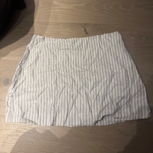 Kjol - Snygg vit kjol med grå ränder, perfekt för en stilren look. Kjolen har en kort längd och är gjord i ett lätt och bekvämt material. Passar bra till både vardag och mer uppklädda tillfällen.