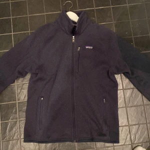 Fleecjacka patagonia - Säljer en mörkblå fleecejacka från Patagonia med dragkedja framtill och två sidofickor. Perfekt för kyliga dagar och har en hög krage för extra värme. Storlek M 