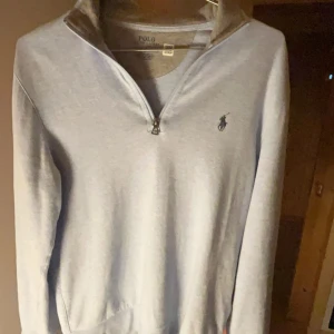 Ljusblå tröja från Polo Ralph Lauren - Säljer en stilren ljusblå tröja från Polo Ralph Lauren med dragkedja vid halsen. Tröjan har en broderad logotyp på bröstet och långa ärmar. Perfekt för en avslappnad och snygg look.