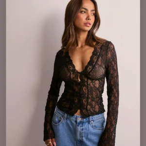Svart spetsblus - Snygg svart spetsblus med långa vida ärmar och v-ringad design. Blusen har knappar framtill och ett genomskinligt mönster som ger en elegant look. Nypris från Nelly är 400kr den är oanvänd 