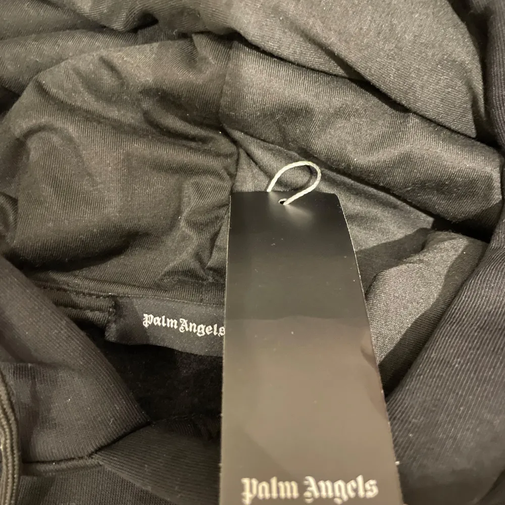 Säljer en svart hoodie från Palm Angels med ett unikt nallebjörnsmotiv på framsidan. Tröjan har en klassisk känguruficka och justerbar huva. Perfekt för en avslappnad stil.. Neuletakit & Villapaidat.