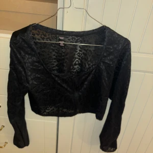Svart leopardmönstrad kofta från Victoria's Secret - Snygg svart kofta från Victoria's Secret med leopardmönster. Den är croppad och har en dragkedja framtill. Perfekt för att ge en edgy touch till din outfit.