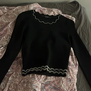 Svart tröja från Guess med vågiga detaljer - Säljer en snygg svart tröja från Guess med unika vågiga kanter i vitt. Blusen har långa ärmar och en stilren design som passar perfekt för en trendig look. Märkesdetalj i metall på baksidan ger en extra touch vilket är ur gulligt! Även perfekt blus för att vara lite mer uppklädd och få en extra touch på outfiten🖤
