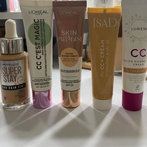 Olika foundations och CC-krämer - Samling av foundations och CC-krämer från Maybelline, L'Oréal, Isadora och Lumene. Inkluderar Super Stay 24H Skin Tint, CC C'est Magic, Skin Paradise, Isadora 3-in-1 CC Cream och Lumene CC Color Correcting Cream. Perfekta för en jämn och strålande hudton. 