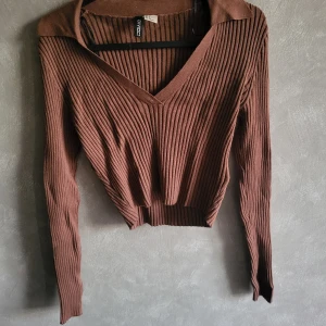 Brun ribbad tröja från Divided - Säljer en snygg brun ribbad tröja från Divided. Tröjan har en v-ringad design och långa ärmar, perfekt för höst och vinter. Den är både stilren och bekväm, idealisk för att hålla sig varm med stil.