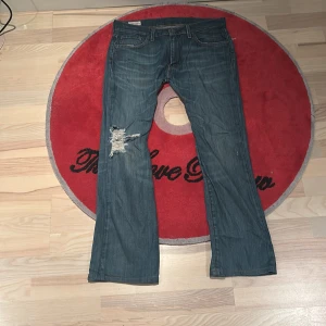Levi's jeans med slitningar - Snygga Levi's jeans i blå denim med slitningar på ena benet. Skriv om du söker mått elr flera bilder!