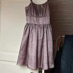 Rosa klänning med glittrigt mönster  - Charmig rosa klänning med glittrande mönster och smala axelband. Den har en smockad rygg för extra komfort och en luftig kjol som ger en fin siluett. Perfekt för speciella tillfällen. Stl 164