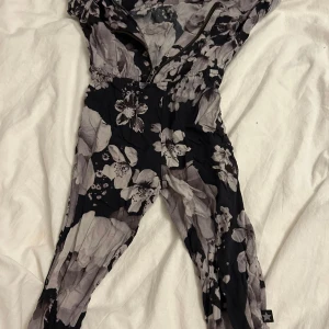 Blommig jumpsuit från Molo - Säljer en snygg blommig jumpsuit från Molo i svart och grått. Den har ett elastiskt band i midjan och korta ärmar. Perfekt för en stilren look! Den kommer tvättas och strykas innan den skickas! ⭐️