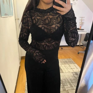 Svart spets jumpsuit - Snygg svart spets suit med svarta ”byxor”. Perfekt för en elegant look med sitt genombrutna mönster och figurnära passform. Knappt använd.