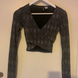 Svart glittrig mönstrad topp från H&M Divided - Suppersnygg svartglittrig mer festlig tröja från H&M Divided. Toppen har en omlott-design med långa ärmar.