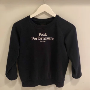 Mörkblå tröja från Peak Performance - Säljer en mörkblå tröja från Peak Performance med vit text på bröstet. Tröjan har långa ärmar och en rund halsringning. Perfekt för en avslappnad stil.