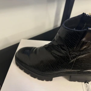 Svarta boots med dragkedja - Snygga svarta boots i skinn med dragkedja på sidan. De har en robust sula med grovt mönster för extra grepp. Perfekta för både stil och funktion.