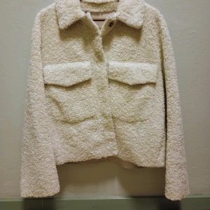 Beige teddyjacka från Zara - Mysig beige teddyjacka från Zara med långa ärmar och två stora fickor framtill. Perfekt för kyligare dagar med sin fluffiga och varma design. Jackan har en klassisk krage och stängs med knappar.