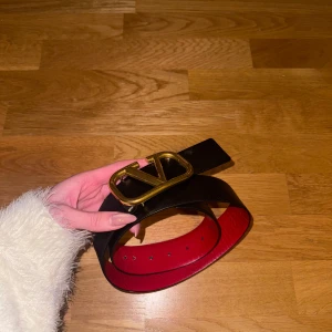 Svart skärp från Valentino - Säljer ett elegant svart skärp från Valentino med en iögonfallande guldspänne. Insidan är röd och skärpet kommer i originalförpackning med tillhörande påse. Perfekt för att lyfta vilken outfit som helst! Äkta och kvitto tillkommer!