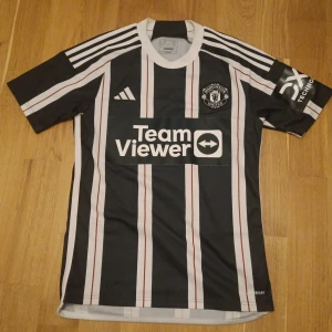 Svart och vit randig fotbollströja från Adidas - Snygg svart och vit randig fotbollströja från Adidas med klubbmärke och sponsorloggor. Kortärmad design med klassiska Adidas-ränder på axlarna. Perfekt för fotbollsfans som vill visa sitt stöd. ÄKTA Skick 9,8/10 Nypris 1500kr säljer för 800 pris kan diskuteras