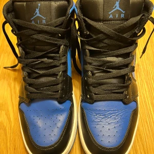 Nike Air Jordans i svart och blått - Snygga Nike Air Jordans i svart och blått med klassisk design. Skorna har snörning och en hög siluett som ger ett sportigt utseende. Perfekta för dig som vill ha en stilren och ikonisk sneaker.