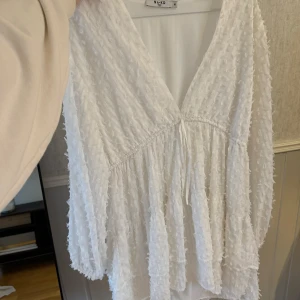 Vit klänning från NA-KD - Säljer en vit klänning från NA-KD med v-ringning och volangdetaljer. Aldrig använd. 