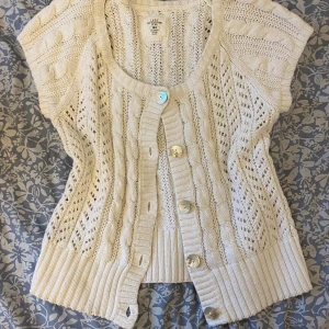 Vit stickad kofta från H&M - Säljer en vit stickad kofta från H&M med vackra flätmönster och stora knappar framtill. Koftan har korta ärmar och ribbade kanter, perfekt för lager-på-lager-stil. Passar utmärkt för både vår och höst. Sitter som storlek L men det står XL på lappen. Jag använder oftast xs-s så den sitter lite större på mig. ❣️❣️