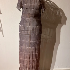 Halvtransparent långklänning från Sisters Point - Grå och brun, elastisk långklänning från Sisters Point med ett randigt mönster. Klänningen har korta ärmar och är tillverkad i ett transparent material som ger en cool look. Perfekt att använda utanpå linne/BH och leggings eller över en lång färgglad klänning. Har några små hål från kattklor som jag såg först när jag synade klänningen. Inget som stör, vill man att det ska se ut som spindelnät så klipp själv 🕸️🕷️Perfekt för att sticka ut med stil! Storlek M/L