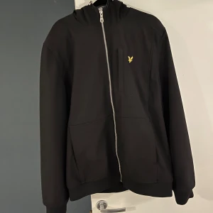 Lyle & Scott jacka  - Snygg svart jacka från Lyle & Scott med dragkedja och deras ikoniska logga på bröstet. Jackan har långa ärmar och praktiska fickor framtill. Perfekt för en stilren look. den är inköpt från deras egen butik för 1600kr.  Säljes för 500 Storlek L  Jackan är mycket skön och skyddar otroligt bra mot både vind och regn