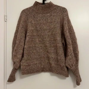 Beige stickad tröja från ONLY - Mysig beige stickad tröja från ONLY med hög krage och långa ärmar. Perfekt för kyliga dagar och ger en avslappnad stil. Tröjan har en ribbad struktur vid krage, ärmslut och nederkant.