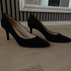 Svarta klackskor  - Eleganta svarta klackskor i mocka med spetsig tå och klack. Perfekta för en stilren look.