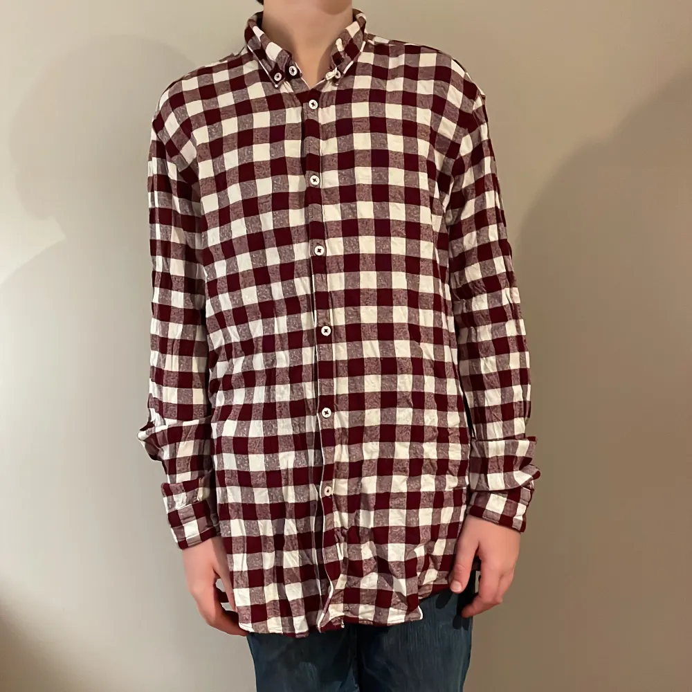 Säljer en rutig skjorta från Zara Man i avslappnad passform. Skjortan har ett klassiskt rutmönster i vinrött och vitt, med långa ärmar och knappar framtill. Perfekt för en stilren och bekväm look.. Paidat.