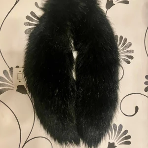 Svart fuskpäls halsduk - Snygg och fluffig svart fuskpäls halsduk som ger en lyxig känsla. Perfekt för att hålla värmen under kyliga dagar. Den har en mjuk och tät struktur som känns skön mot huden.